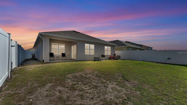 back of house at dusk with a patio area, a fenced backyard, a lawn, and stucco siding