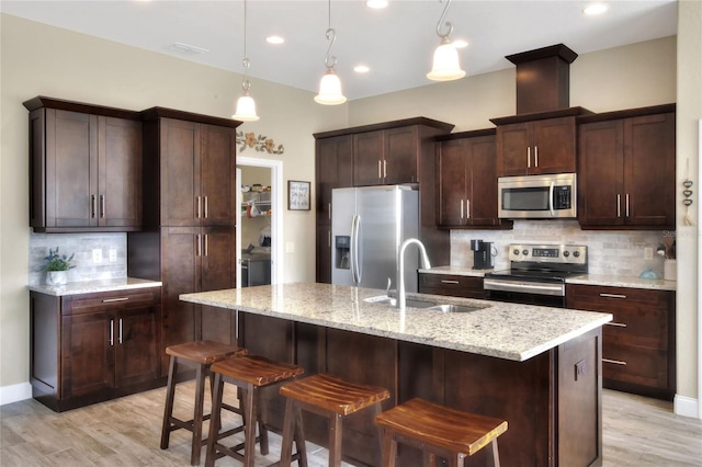 kitchen with dark brown cabinetry, sink, hanging light fixtures, a center island with sink, and appliances with stainless steel finishes