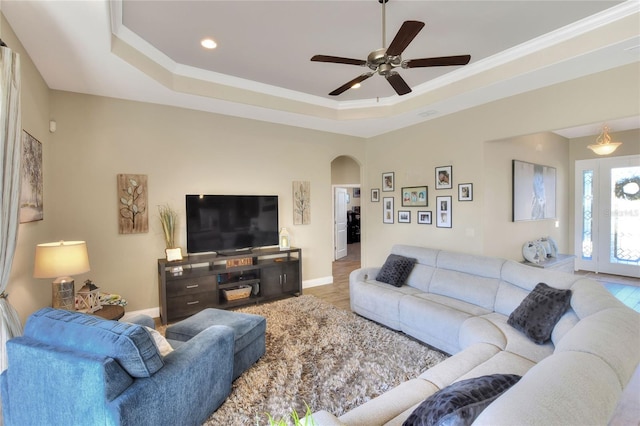 living room with a raised ceiling, ornamental molding, ceiling fan, and light hardwood / wood-style flooring