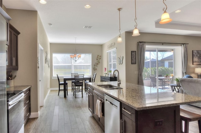 kitchen with pendant lighting, sink, appliances with stainless steel finishes, a kitchen island with sink, and dark brown cabinets