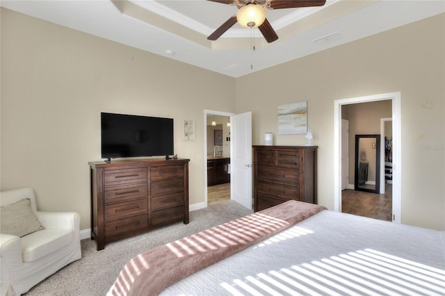 carpeted bedroom with ensuite bathroom, ceiling fan, and a tray ceiling