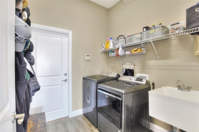 clothes washing area featuring washing machine and dryer, sink, and light hardwood / wood-style flooring