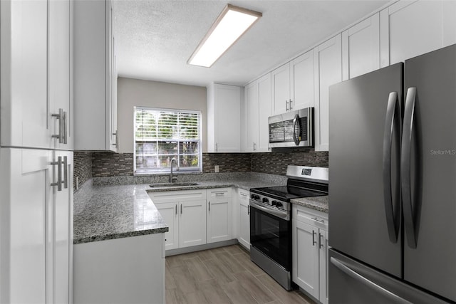 kitchen featuring sink, appliances with stainless steel finishes, white cabinetry, dark stone countertops, and tasteful backsplash