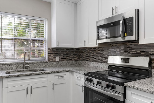 kitchen with sink, appliances with stainless steel finishes, white cabinetry, light stone countertops, and decorative backsplash