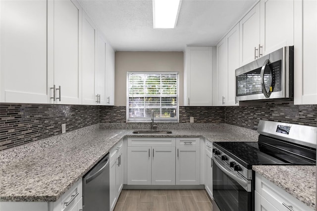 kitchen featuring sink, white cabinetry, light stone counters, tasteful backsplash, and stainless steel appliances