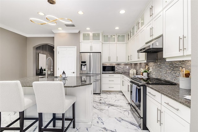 kitchen with appliances with stainless steel finishes, a breakfast bar, dark stone countertops, white cabinets, and a center island with sink