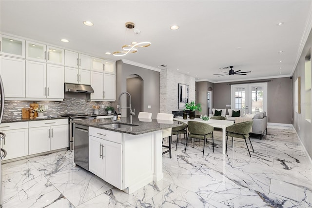 kitchen with pendant lighting, an island with sink, sink, dark stone counters, and crown molding