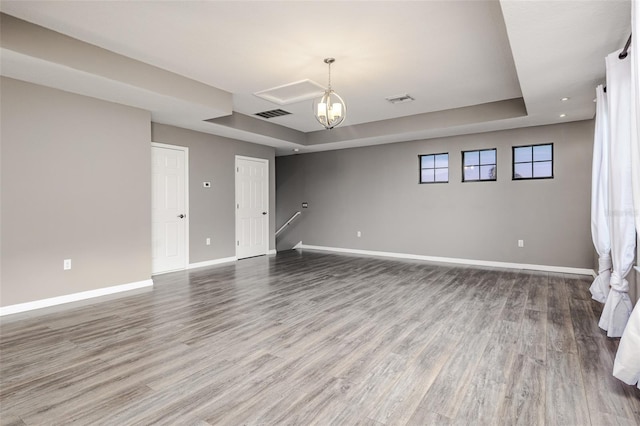 empty room featuring wood-type flooring, a chandelier, and a tray ceiling