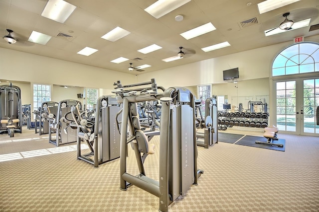 workout area featuring ceiling fan, a towering ceiling, a drop ceiling, light carpet, and french doors