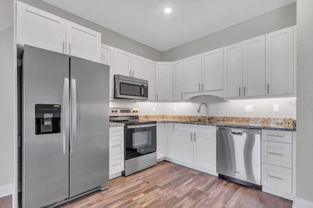 kitchen with sink, white cabinetry, light stone counters, stainless steel appliances, and hardwood / wood-style floors