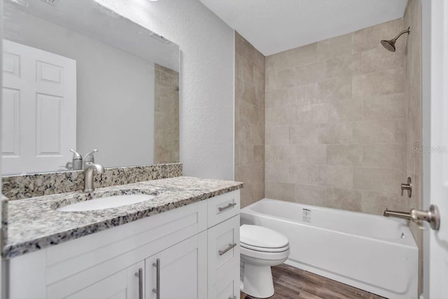 full bathroom with hardwood / wood-style flooring, tiled shower / bath, vanity, and toilet