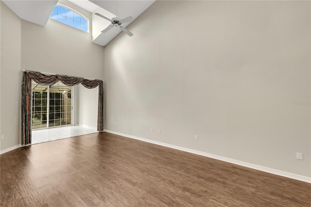 spare room featuring a ceiling fan, a high ceiling, baseboards, and wood finished floors