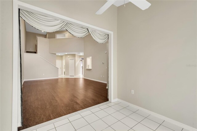 unfurnished room featuring a towering ceiling, light tile patterned floors, ceiling fan, and baseboards