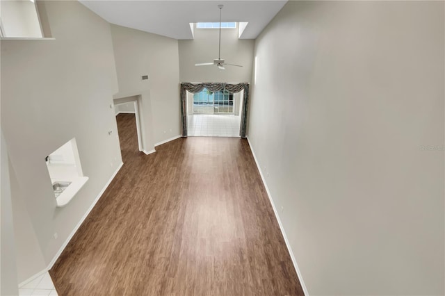 unfurnished living room with a towering ceiling, a skylight, baseboards, and wood finished floors