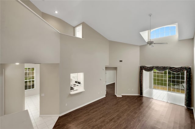 unfurnished living room featuring high vaulted ceiling, a healthy amount of sunlight, baseboards, and wood finished floors