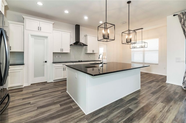 kitchen featuring a center island with sink, wall chimney exhaust hood, hanging light fixtures, and white cabinets