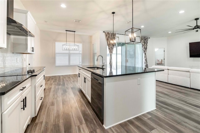 kitchen with white cabinetry, sink, hanging light fixtures, wall chimney range hood, and a center island with sink