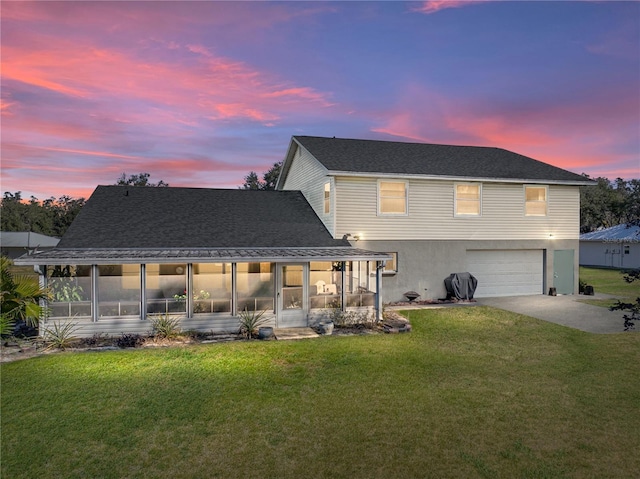 back house at dusk with a garage, a sunroom, and a lawn