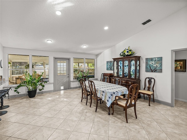dining area featuring vaulted ceiling, a textured ceiling, and light tile patterned floors
