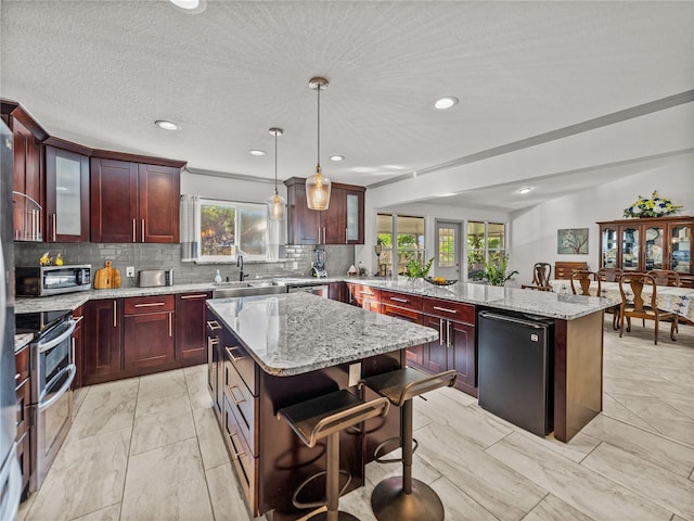 kitchen featuring a breakfast bar, light stone counters, a center island, hanging light fixtures, and appliances with stainless steel finishes