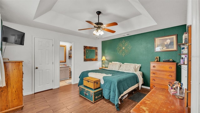 bedroom with connected bathroom, a tray ceiling, ceiling fan, and light wood-type flooring