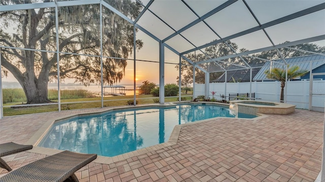 pool at dusk featuring an in ground hot tub, a lanai, and a patio