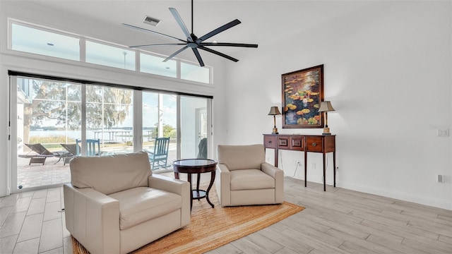 living area featuring a towering ceiling, ceiling fan, and light wood-type flooring