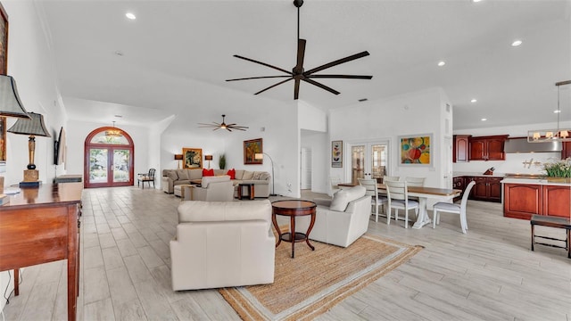 living room featuring a towering ceiling, light hardwood / wood-style flooring, ceiling fan, and french doors