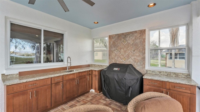 kitchen featuring light stone counters, ceiling fan, and sink