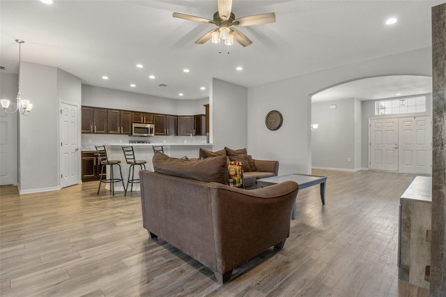 living room featuring ceiling fan with notable chandelier and light wood-type flooring