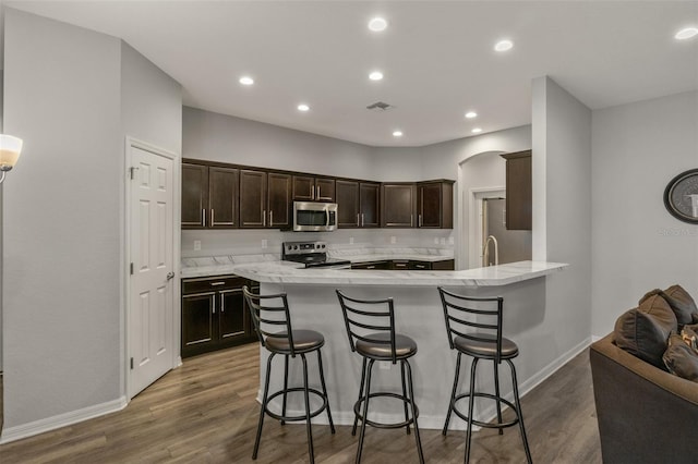 kitchen with appliances with stainless steel finishes, dark hardwood / wood-style flooring, kitchen peninsula, and a breakfast bar area