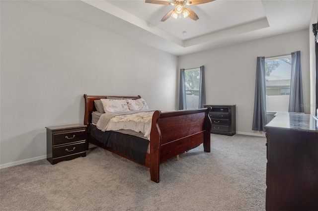 bedroom with ceiling fan, light colored carpet, and a raised ceiling