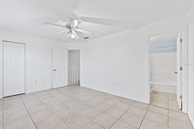 unfurnished bedroom featuring light tile patterned flooring, ensuite bathroom, ceiling fan, a textured ceiling, and a closet