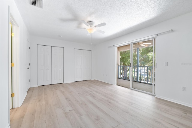 unfurnished bedroom with access to exterior, two closets, a textured ceiling, and light wood-type flooring