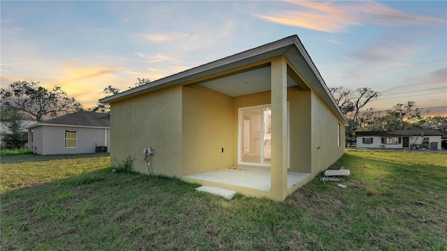 back house at dusk featuring a patio, central air condition unit, and a lawn