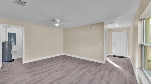 unfurnished room featuring electric panel, water heater, ceiling fan, and light wood-type flooring