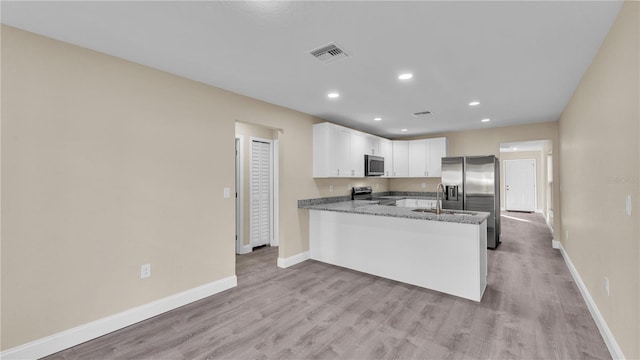 kitchen with appliances with stainless steel finishes, white cabinetry, dark stone counters, kitchen peninsula, and light wood-type flooring