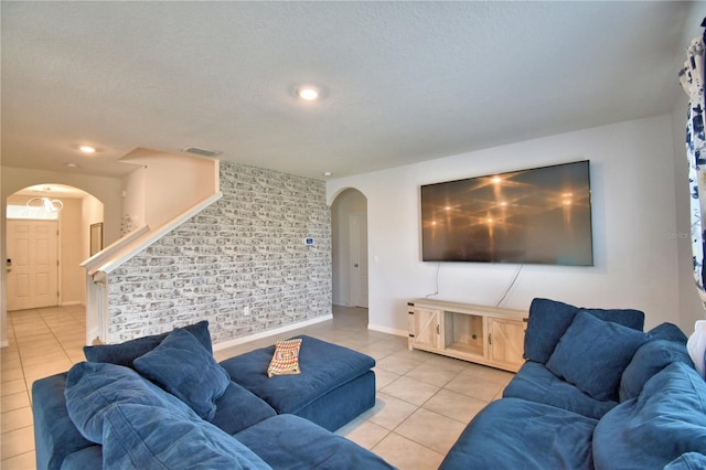 living room with brick wall, a textured ceiling, and light tile patterned flooring