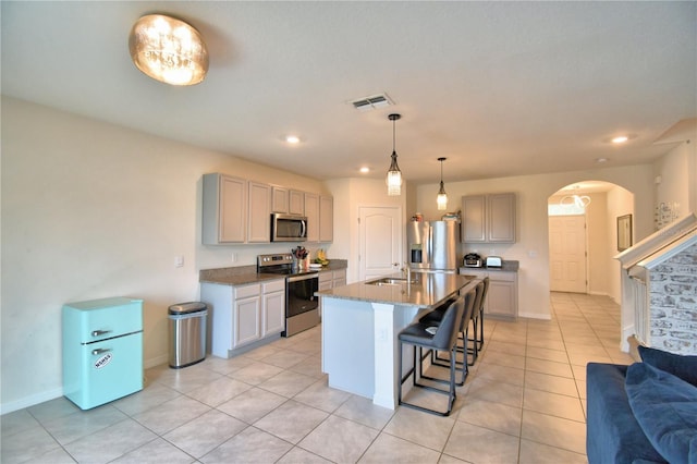 kitchen with sink, gray cabinets, a breakfast bar, stainless steel appliances, and an island with sink