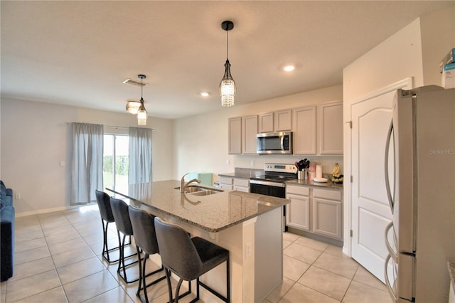 kitchen featuring sink, a center island with sink, pendant lighting, stainless steel appliances, and light stone countertops