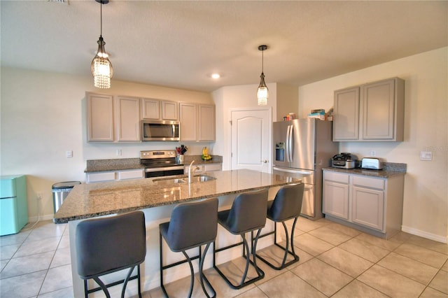 kitchen featuring stainless steel appliances, a kitchen island with sink, pendant lighting, and gray cabinets