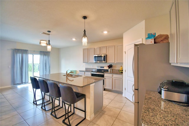 kitchen featuring sink, light stone counters, hanging light fixtures, a center island with sink, and stainless steel appliances