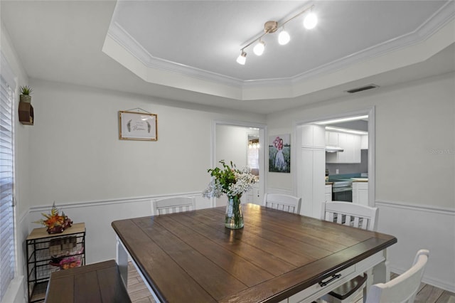 dining area featuring a tray ceiling, ornamental molding, rail lighting, and light wood-type flooring