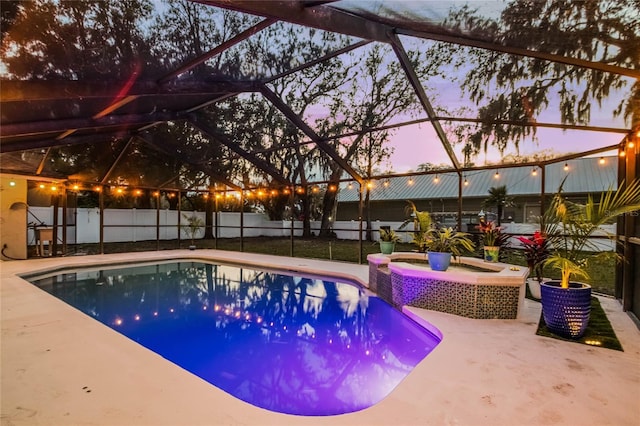 pool at dusk featuring an in ground hot tub, a patio, and glass enclosure