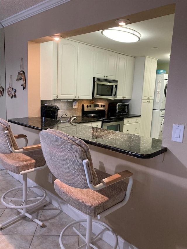 kitchen with stacked washer and dryer, a breakfast bar area, white cabinetry, appliances with stainless steel finishes, and kitchen peninsula