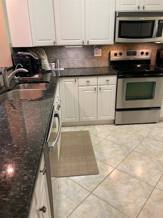 kitchen featuring sink, white cabinetry, dark stone counters, stainless steel appliances, and backsplash