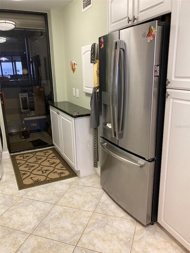 kitchen with light tile patterned flooring, dark stone countertops, stainless steel fridge, and white cabinets