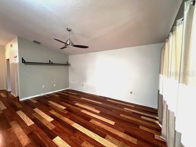 unfurnished living room featuring ceiling fan, dark hardwood / wood-style floors, vaulted ceiling, and a textured ceiling