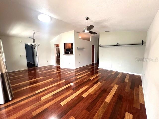 unfurnished living room with vaulted ceiling, ceiling fan with notable chandelier, and dark hardwood / wood-style flooring