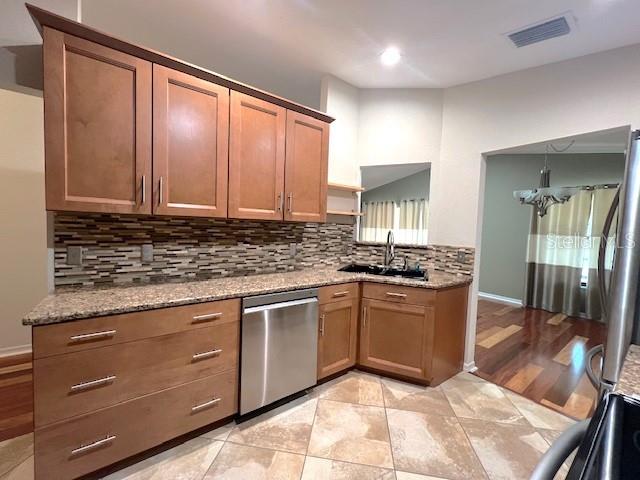 kitchen with appliances with stainless steel finishes, stone countertops, sink, decorative backsplash, and a notable chandelier